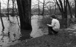 Woman crouching by Red Cedar River to feed the ducks